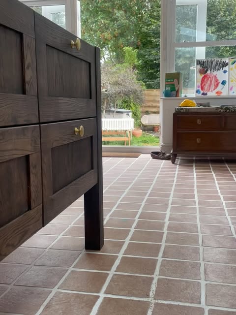 A dark oak shaker kitchen island with drawers and oak newel post legs on a terracotta tiled floor