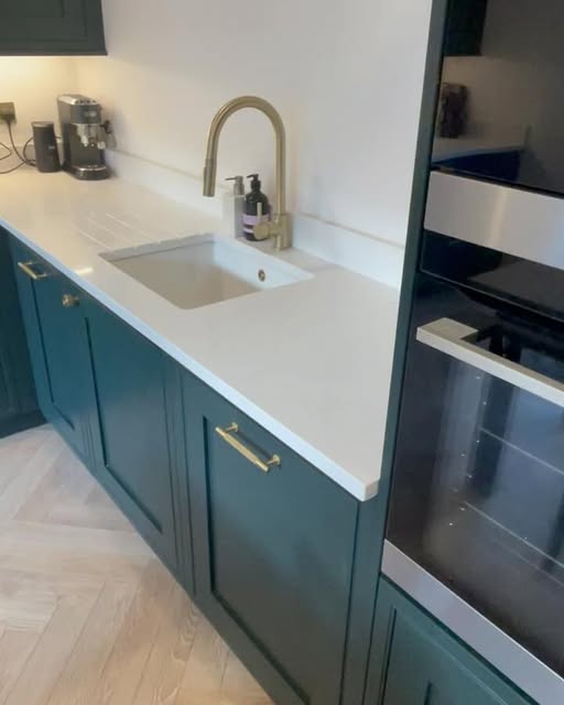 Close-up of heritage green shaker units with brass handles and a white quartz worktop